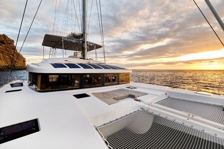 Solar powered catamaran at sunset, fully sustainable and powered by solar energy, charging batteries aboard a sailboat, vessel in ocean waters, nobody. Photovoltaic panels renewable eco energy conceptの写真素材