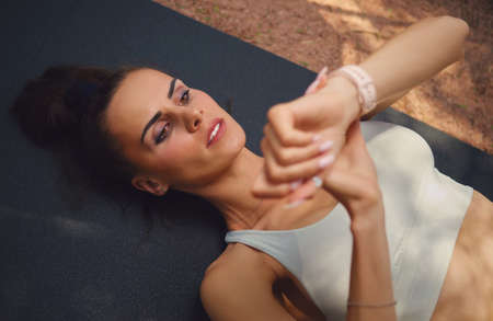 Top close up view young woman in sporty top lying on mat timing start finish work out sportive training outdoor looks at wristwatch. Healthy lifestyle, sport training activity use modern tech conceptの写真素材