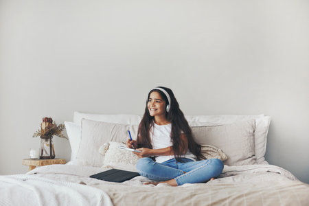 Beautiful pre-teen 12s girl in headphones listen audio course, e-studying seated on bed in bedroom alone at home. Homeschooling using modern tech, on-line class, modern wireless tech usageの写真素材