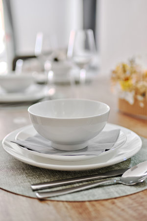 Close up white porcelain tableware plates on place mats and empty wine glasses ready for dinner. Table settings wait for guests at home or restaurant. No peopleの写真素材