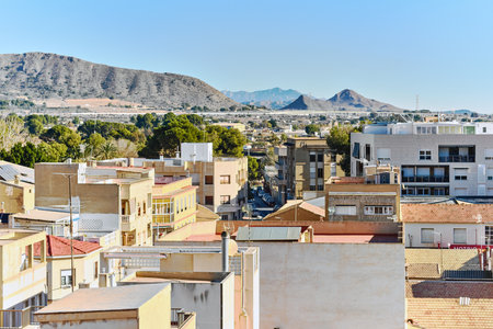 Novelda townscape with mountains view in background. Buildings rooftops, with clear blue skies and the mountainous terrain, typical Mediterranean architecture town, province of Alicante, Spainの写真素材