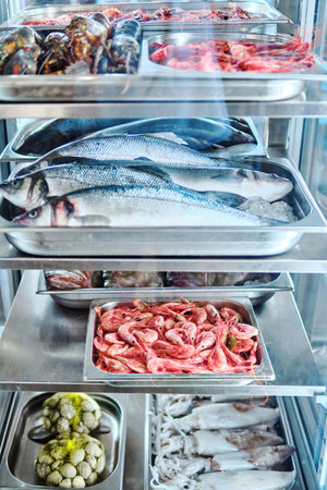 Variety of seafood displayed in trays inside refrigerated glass caseの写真素材