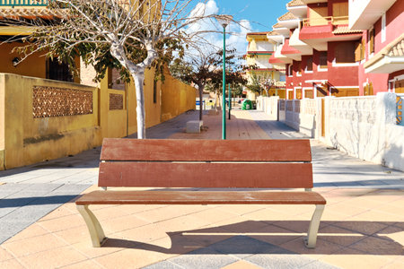 View to the wooden bench in the quiet residential sunny Torre de la Horadada town, Mediterranean neighborhood. Costa Blanca, province of Alicante, Spainの写真素材