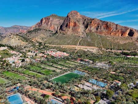Aerial view of Palmeral de Orihuela or palm grove, lush green oasis amidst urban sprawl and mountainous backdrop under clear Spanish skyの写真素材