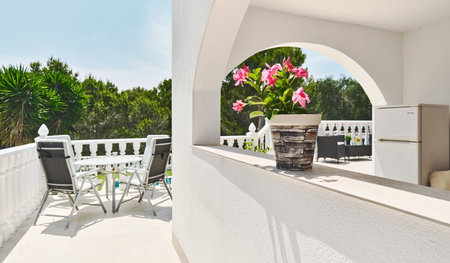 Bright Mediterranean-style terrace framed by white arches and balustrades. Relaxing outdoor setting with lush green trees in background during summer sunny dayの写真素材