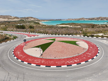 Scenic roundabout with colorful landscaping, modern road markings, located near a turquoise reservoirの写真素材