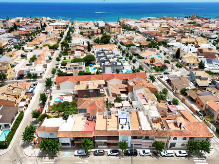 Aerial view of Mediterranean coastal town of Torre de la Horadada with traditional Spanish houses, tiled rooftops, narrow streets, green trees, and sparkling sea in background on sunny day. Spainの写真素材
