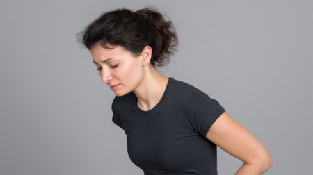 The image features a young woman exhibiting a look of discomfort while standing against a simple gray background, conveying an emotional struggle.の素材