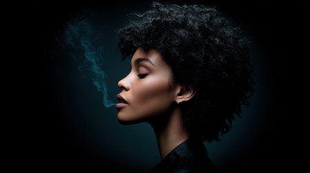 This artistic portrait features a confident woman with afro hair exhaling smoke in a dark studio, showcasing dramatic lighting and striking shadows, creating a serene and expressive atmosphere.の素材