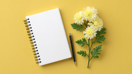 A blank notebook with a spiral binding lies next to a cluster of yellow flowers, all set against a bright yellow background, perfect for inspiration.の素材