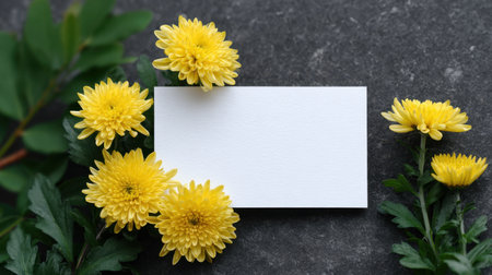 A beautiful display featuring fresh yellow chrysanthemums, complemented by a blank card on a textured stone background, perfect for creative projects.の素材