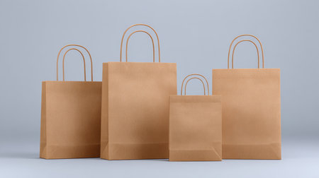 A collection of four brown paper bags in various sizes, arranged on a sleek gray background, perfect for showcasing shopping, gifting, or packaging ideas.の素材