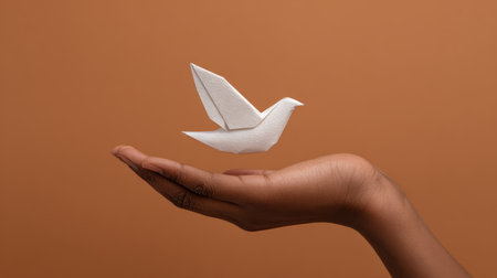 This captivating image features a delicate paper bird gracefully balancing on the palm of a hand against a warm brown background, symbolizing peace and freedom.の素材