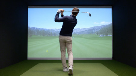 A golfer practicing their swing in a modern indoor golf simulator, featuring a vibrant virtual landscape on screen and a focus on technique and performance.の素材