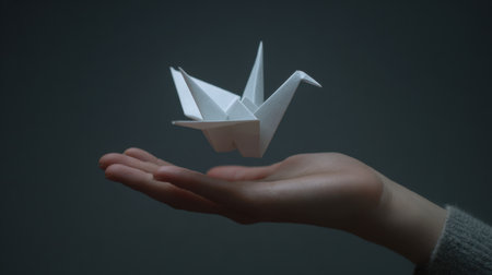 A serene image of a hand supporting a paper crane that appears to float gracefully above it, capturing themes of art, peace, and creativity.の素材