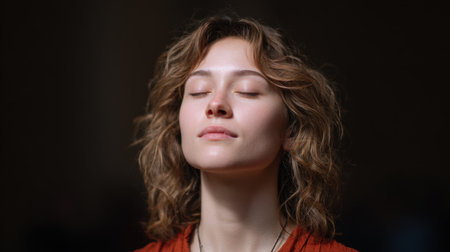 A young woman with curly brown hair meditates with her eyes closed, showcasing a serene expression. The warm light enhances the tranquil atmosphere, inviting feelings of peace and mindfulness.の素材