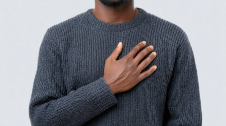 This image features a man wearing a gray sweater, placing his hand on his heart against a neutral background, symbolizing commitment and sincerity.の素材