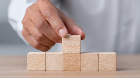 A close-up view of a hand carefully stacking wooden blocks on a table, showcasing creativity and strategic organization in a minimalist workspace.の素材