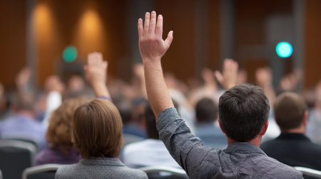 An engaged audience at a conference raises their hands to ask questions and give feedback during a seminar in a professional setting.の素材