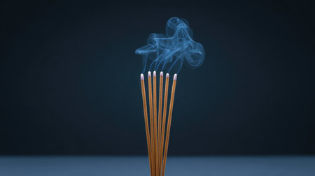 A striking close-up view of incense sticks gracefully releasing soft wisps of smoke against a dark backdrop, evoking feelings of calm and serenity.の素材