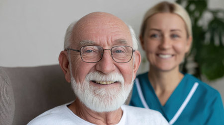 A joyful elderly man smiles warmly while sitting in a comfortable chair. His caregiver stands behind him, reflecting a positive, caring relationship that emphasizes companionship and support in a bright, inviting setting.の素材