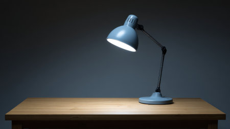 A modern desk lamp sits on a wooden table, providing soft illumination in a dark setting, perfect for enhancing workspace ambiance and focus.の素材