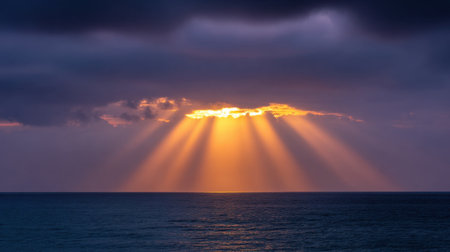 A breathtaking view of sunlight breaking through dark clouds over calm ocean waters, showcasing brilliant colors and a serene atmosphere at dusk.の素材