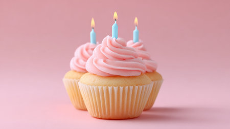 This image features three beautifully frosted cupcakes topped with blue candles, set against a soft pink background. Perfect for birthdays and celebrations.の素材