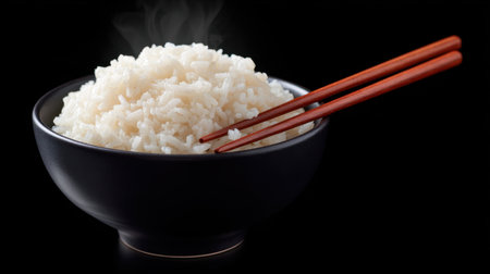 A steaming bowl of fragrant white rice sits against a black background, accompanied by wooden chopsticks, perfect for any meal or occasion.の素材
