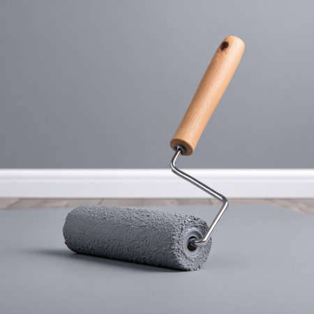 A close-up shot of a paint roller with a wooden handle set against a smooth gray background, perfect for showcasing home renovation projects or DIY tasks.の素材