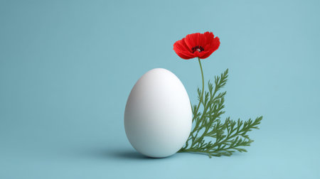 A striking white egg paired with a vibrant red flower and lush green foliage against a soft blue background, evoking a sense of spring and freshness.の素材