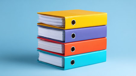 This image features a stack of colorful binders in vibrant tones, perfect for organizing documents. The light blue backdrop highlights the binders, ideal for office and educational contexts.の素材