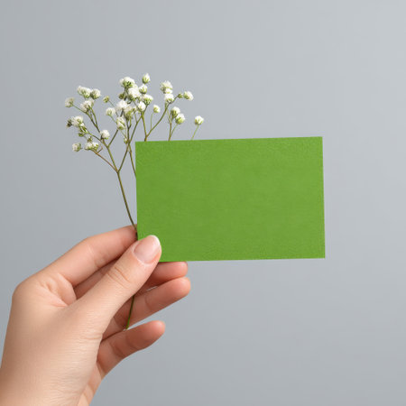 A hand gracefully holds a flat green card accompanied by a delicate white flower, perfect for showcasing minimalist design and creative concepts.の素材