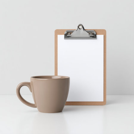 A stylish brown coffee mug sits beside a blank clipboard on a minimalist desk, creating a serene and modern workspace atmosphere perfect for productivity.の素材