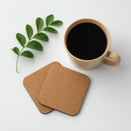 This serene image captures a cozy coffee moment, featuring a cup of black coffee beside cork coasters and a green leaf, all on a minimalist white surface.の素材