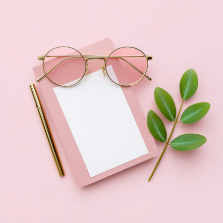 A stylish flat lay composition featuring round glasses, a blank notebook, a gold pen, and a green leaf on a soft pink background, perfect for creative inspiration.の素材