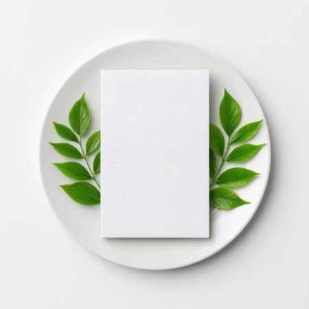 A blank white card sits elegantly on a minimalist plate, surrounded by fresh green leaves, creating a perfect canvas for creative design or presentation.の素材