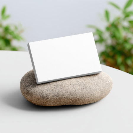 A minimalist blank business card sits atop a smooth stone, set in a serene outdoor environment surrounded by lush greenery, evoking simplicity and elegance.の素材