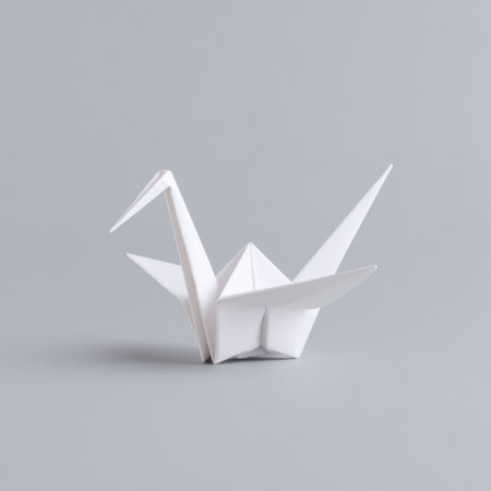 This image features an elegant white origami crane crafted from paper, set against a smooth gray background. The intricate folds and minimalist design create a tranquil and artistic ambiance, symbolizing peace and harmony.の素材