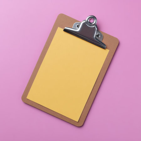 A blank yellow paper positioned on a brown clipboard set against a vibrant pink background. Ideal for creative projects, note-taking, or office designs.の素材