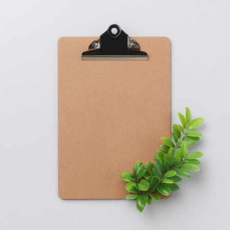 The image features a brown clipboard accompanied by vibrant green leaves against a clean white backdrop, ideal for workspace inspiration and organization.の素材