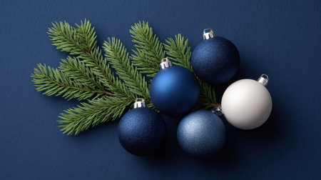A beautiful arrangement of blue and white Christmas ornaments resting on a fresh green pine branch against a deep blue background, perfect for holiday decor.の素材