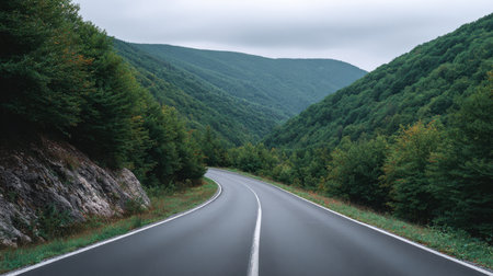 A winding road gracefully curves through a vibrant green mountain landscape. The tranquil atmosphere is enhanced by an overcast sky, perfect for travel.の素材