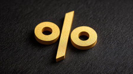 A close-up view of a golden percentage symbol placed on a dark stone background, representing financial calculations, discounts, and marketing strategies.の素材
