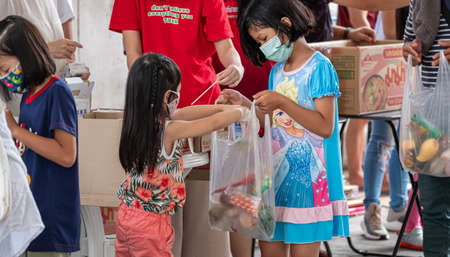 Due to pandemic,Families with face mask impacted by Coronavirus get their free food distribution offered by benevolents. The girl get her share happily.のeditorial素材