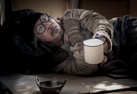 Due to the   pandemic the homeless man lives by the walkway and begs for donation. He suffers from hunger, holds out his hand and mug.の写真素材