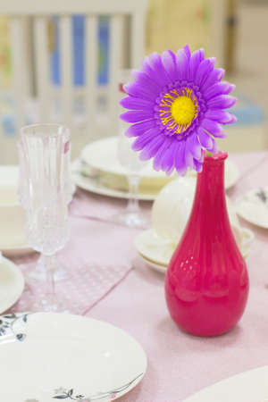 Bright artificial flower in a vase on laid table