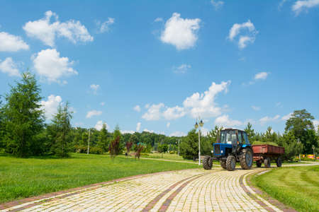 Tractor-trailer with grass stands in the road in the park