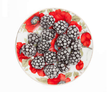 Frozen blackberries covered with frost on a bright plate isolated on whiteの写真素材