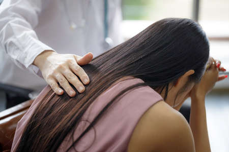 Asian male psychiatrist puts his hand on the shoulder of a young woman to give encouragement as she is worried by the spread  . Disease symptoms talk about health care conceptの写真素材